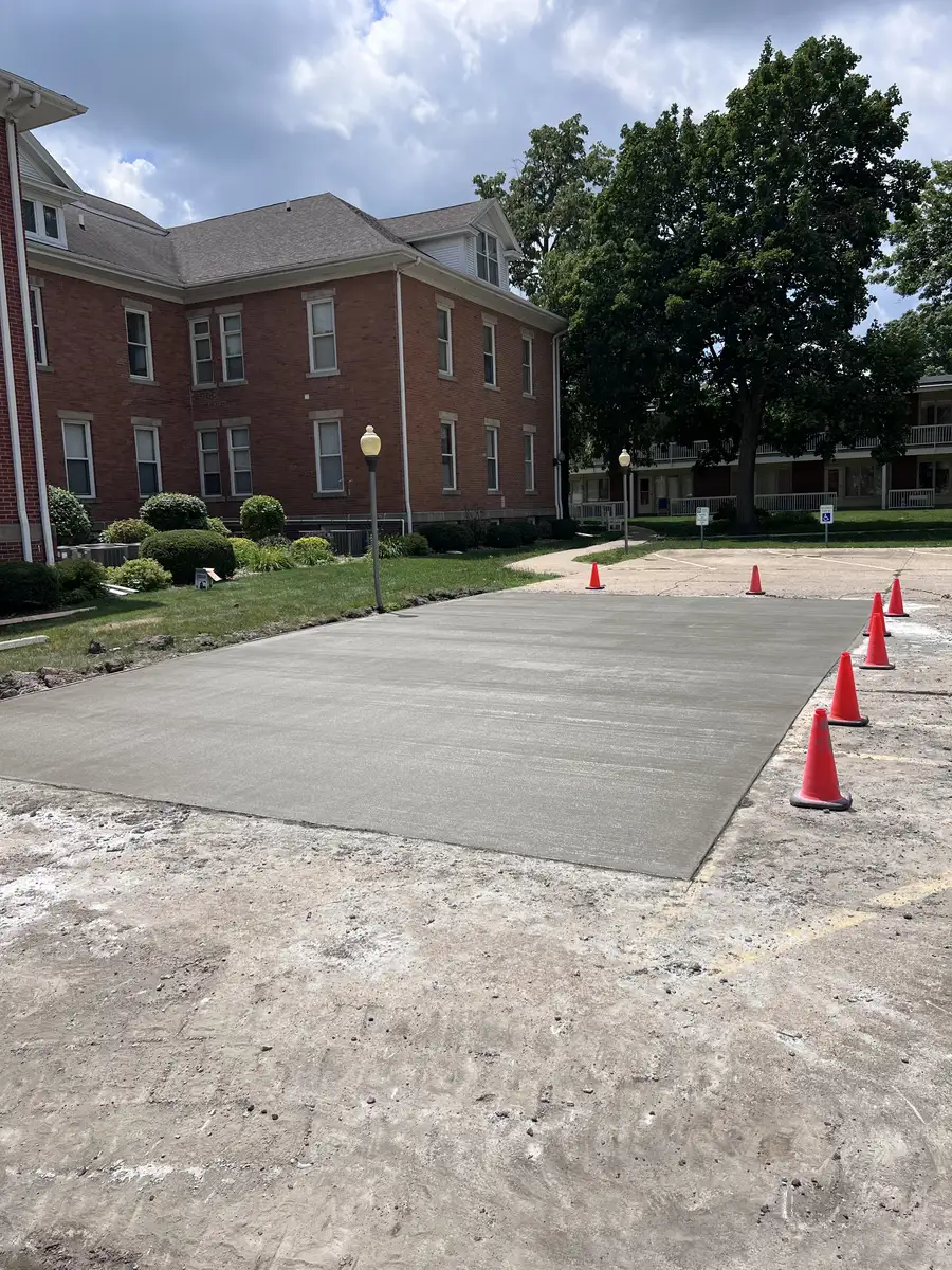 Concrete slab poured beside a brick apartment building, cones around the fresh pour