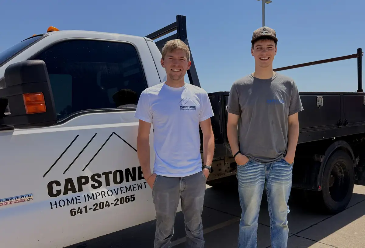 Two Capstone crew members standing by the white truck lettered Capstone Home Improvement 641-204-2065