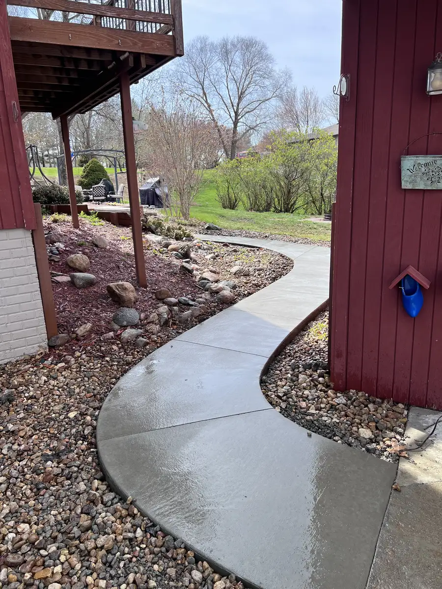 Curved concrete sidewalk running through landscape rock beside a red house