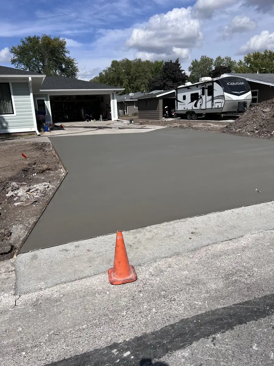 Freshly poured concrete driveway in front of a house, with an orange cone at the curb