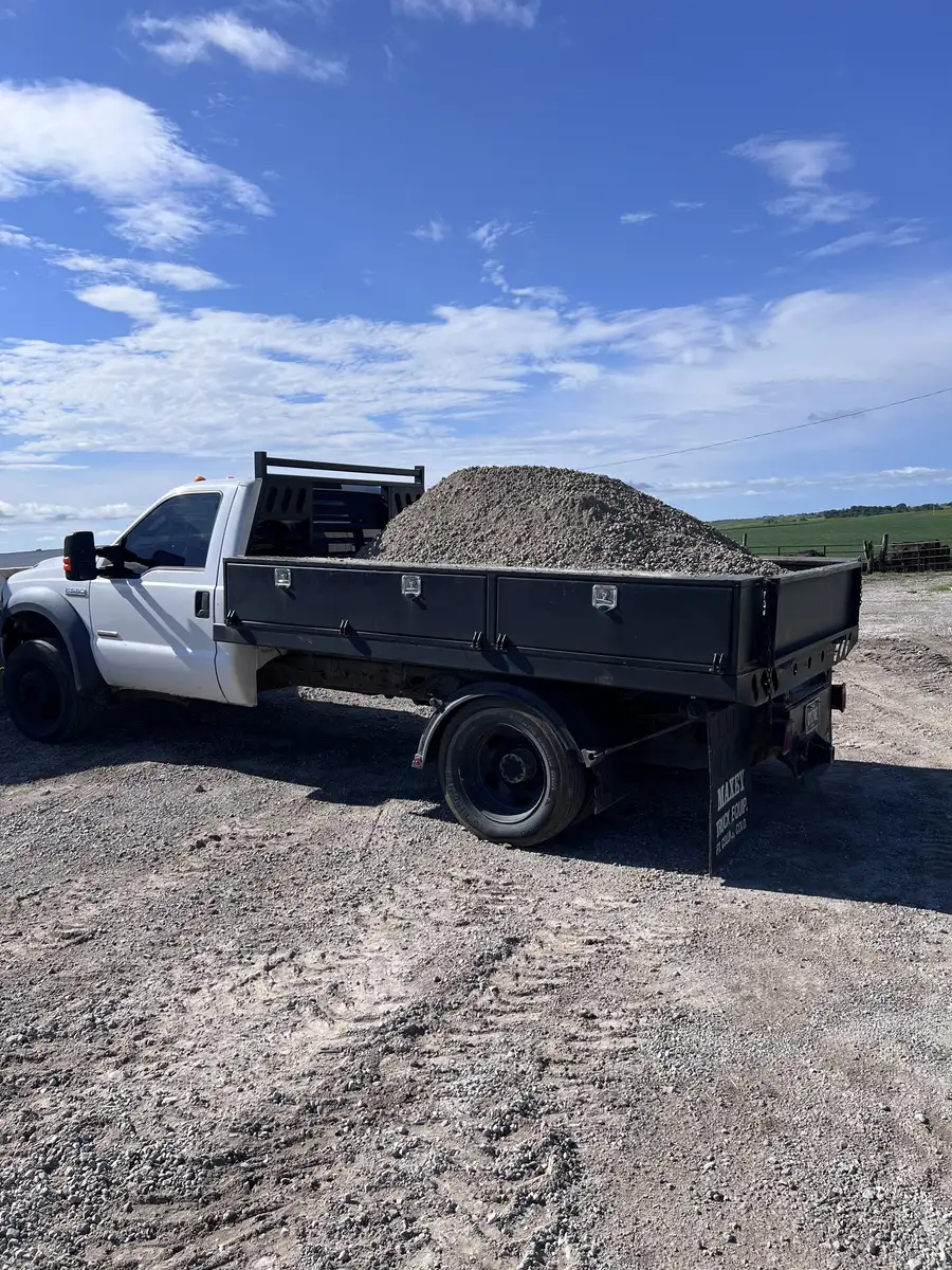 Capstone flatbed truck loaded with gravel next to a farm field