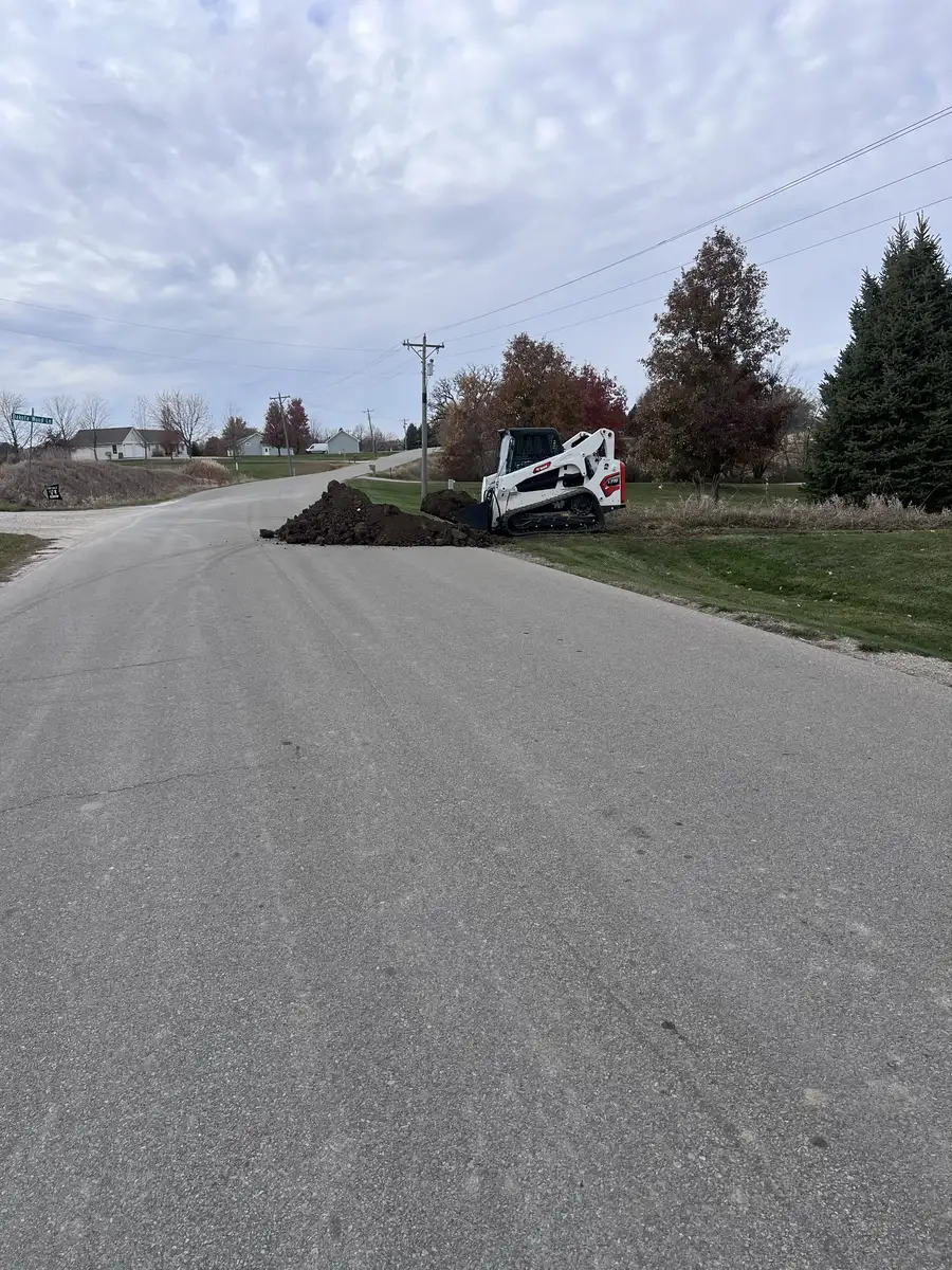 Bobcat skid steer doing dirt work in the ditch beside a paved road