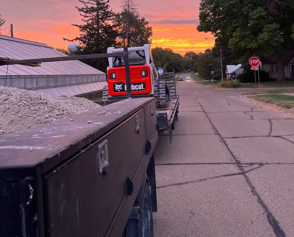 Capstone truck and Bobcat on a trailer at sunset, loaded with gravel